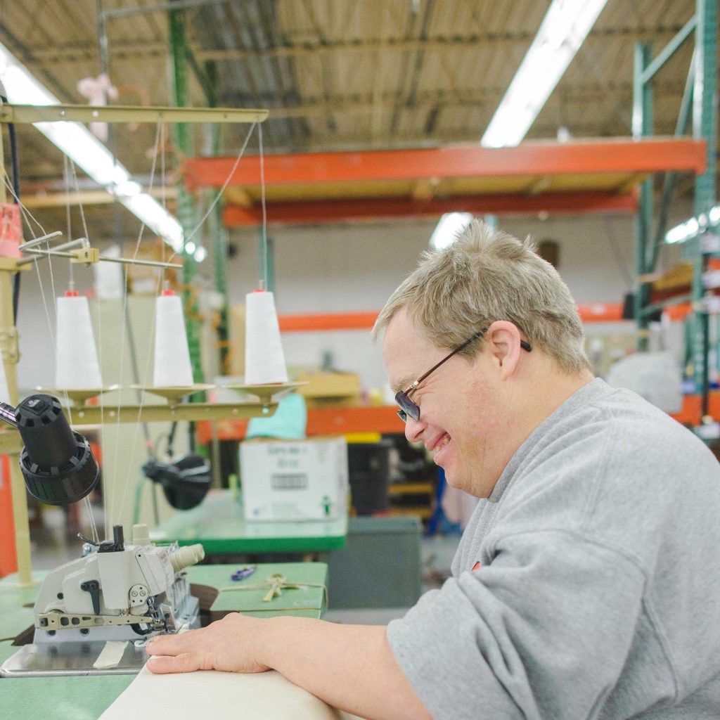 An adult man with disabilities smiling as he folds fabric.