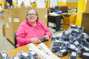 A woman in a pink shirt packaging and labeling leather belts.